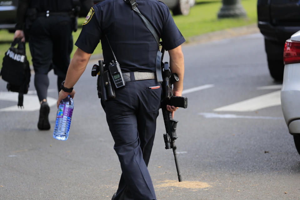 A Honolulu police officer carries an assault rifle near the scene of multiple house fires in a Diamond Head neighborhood, Sunday, Jan. 19, 2020, in Honolulu, following a shooting in which two police officers were shot. (AP Photo/Marco Garcia)