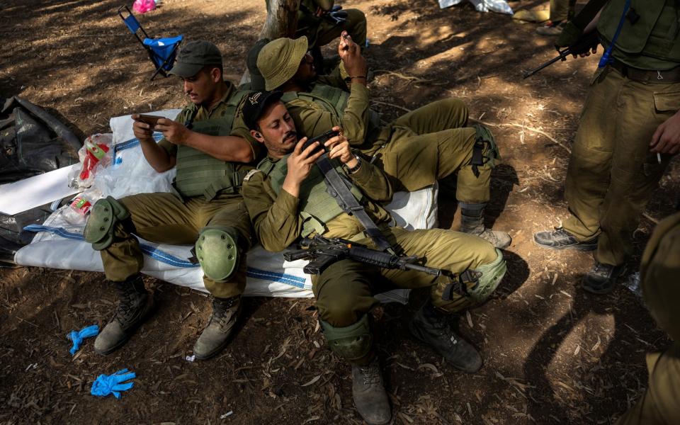 Israeli soldiers take a break after cleaning debris and personal items left behind at the site of the surprise attack launched by Hamas on October 7