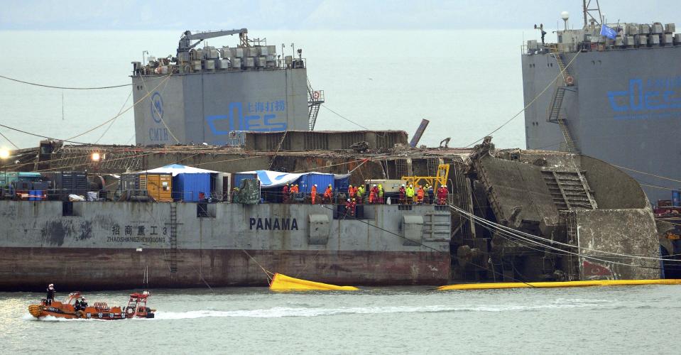 Workers try to raise the sunken Sewol ferry between two barges during the salvage operation in waters off Jindo, South Korea, Friday, March 24, 2017. South Korean efforts to bring the sunken, 6,800-ton ferry back to land cleared an obstacle on Friday after divers cut off a vehicle ramp that had been dangling from the ship and hindering efforts to raise it. (Gang Jong-min/Newsis via AP)