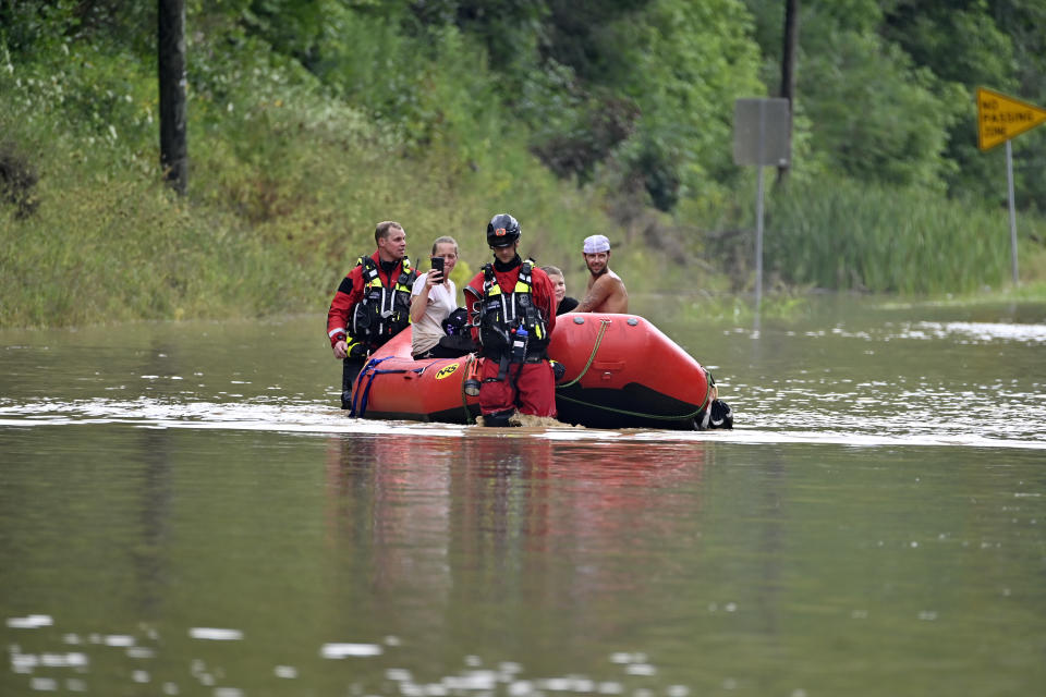 FILE - Members of the Winchester, Ky., Fire Department walk inflatable boats across flood waters over a road in Jackson, Ky., to pick up people stranded by the floodwaters on Thursday, July 28, 2022. The same stubborn weather system caused intense downpours in St. Louis and Appalachia that led to devastating and in some cases deadly flooding. (AP Photo/Timothy D. Easley, File)