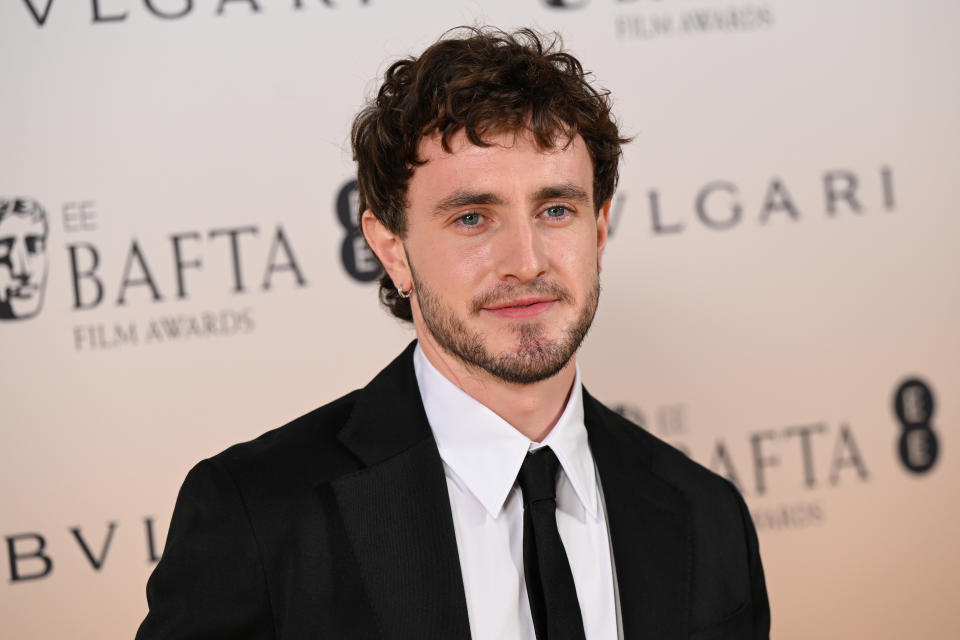 Paul Mescal wearing a black suit and tie poses on the red carpet at the BAFTA event. The background features BAFTA and Bulgari logos