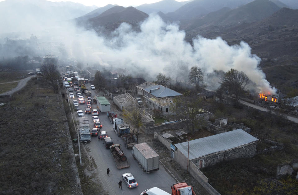Smoke rises from a burning house as cars and trucks stuck in a huge traffic jam climbing along the road from Kalbajar leaving the separatist region of Nagorno-Karabakh to Armenia, on Saturday, Nov. 14, 2020. The territory is to be turned over to Azerbaijan on Sunday as part of territorial concessions in an agreement to end six weeks of intense fighting with Armenian forces. Hundreds of thousands of Azeris were displaced by the war that ended in 1994. It is unclear when any civilians might try to settle in Karvachar — which will now be known by its Azeri name Kalbajar — or elsewhere. (AP Photo/Dmitry Lovetsky)
