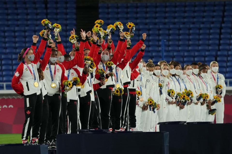 Canada women's soccer players celebrate their Olympic gold medal while members of the bronze medalist USA look on.