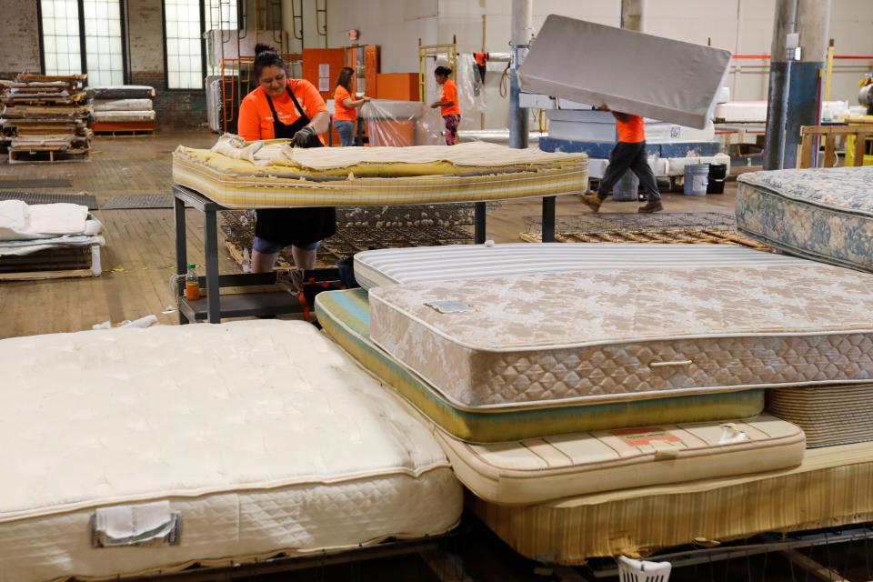 Julia Martinez breaks down a used mattress into its various parts, as other HandUp Mattress Recycling & Upcycling workers move mattresses to be reconditioned into a cleaning station at the facility in the Kilburn Mill in New Bedford.
