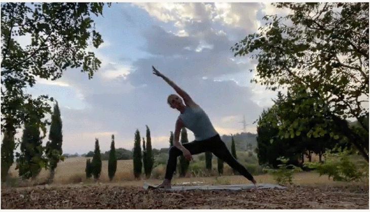 Woman practicing yoga outside at sunrise with a bent front knee and her top arm extending