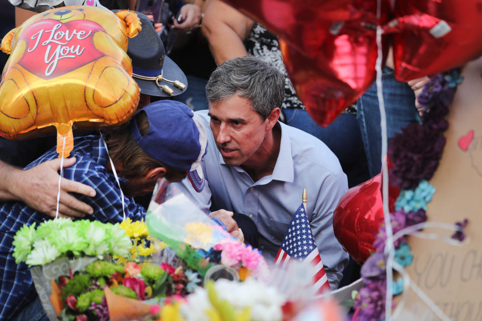 Beto O'Rourke crouches next to Antonio Basco amid flowers, an American flag, balloons, one of which reads: I love you, and other people.