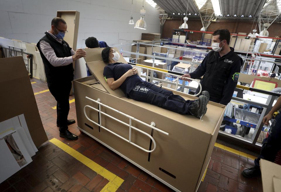 Rodolfo Gomez, left, and his employees demonstrate how their design of a cardboard box can serve as both a hospital bed and a coffin, designed for COVID-19 patients, in Bogota, Colombia, Friday, May 8, 2020. Gomez said he plans to donate the first units to Colombia's Amazonas state, and that he will sell others to small hospitals for 87 dollars. (AP Photo/Fernando Vergara)