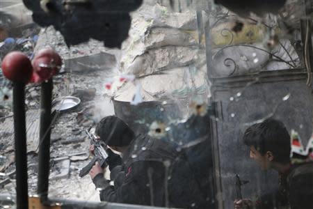 A Free Syrian Army fighter, seen through a mirror riddled with bullets, fires his weapon towards forces loyal to Syria's President Bashar al-Assad in Aleppo's Sheikh Maqsoud neighbourhood, February 16, 2014. REUTERS/Hosam Katan