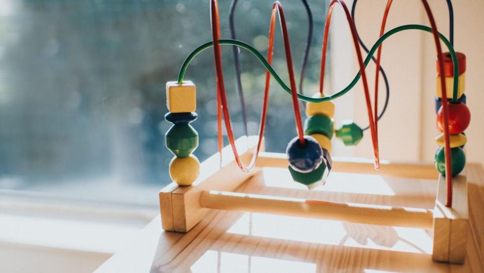 A colourful children's bead toy sits on a window ledge in the sunlight