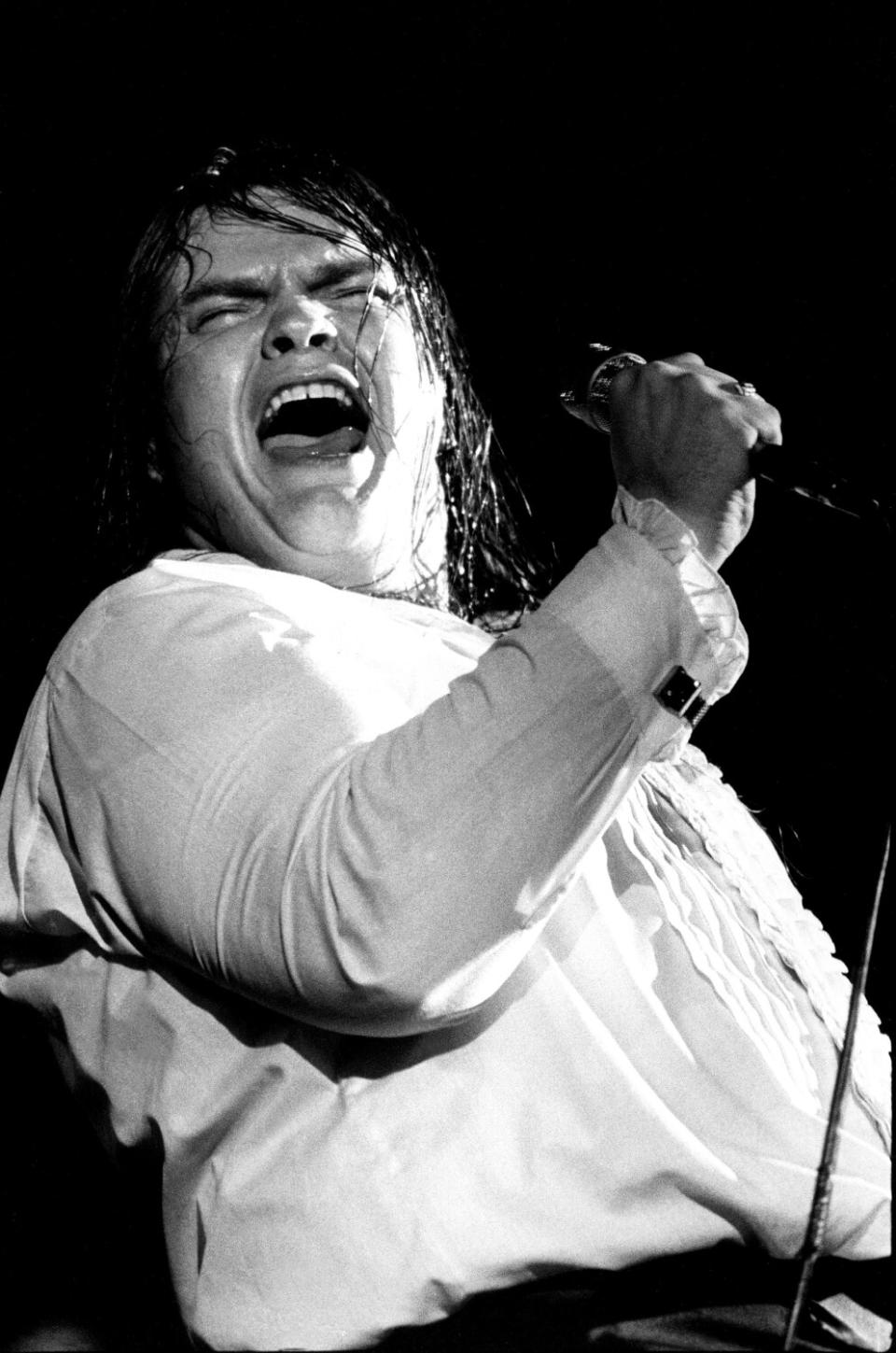 A black and white photo of a man belting onstage