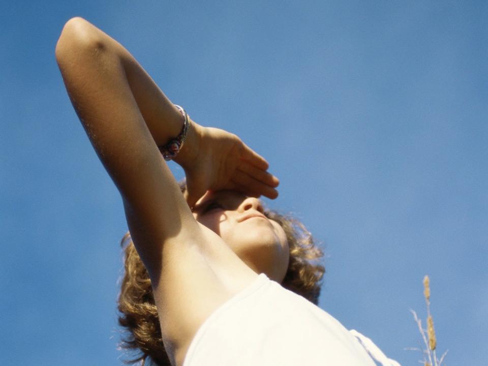 A woman uses her hand to shield her eyes, revealing her arm pit.