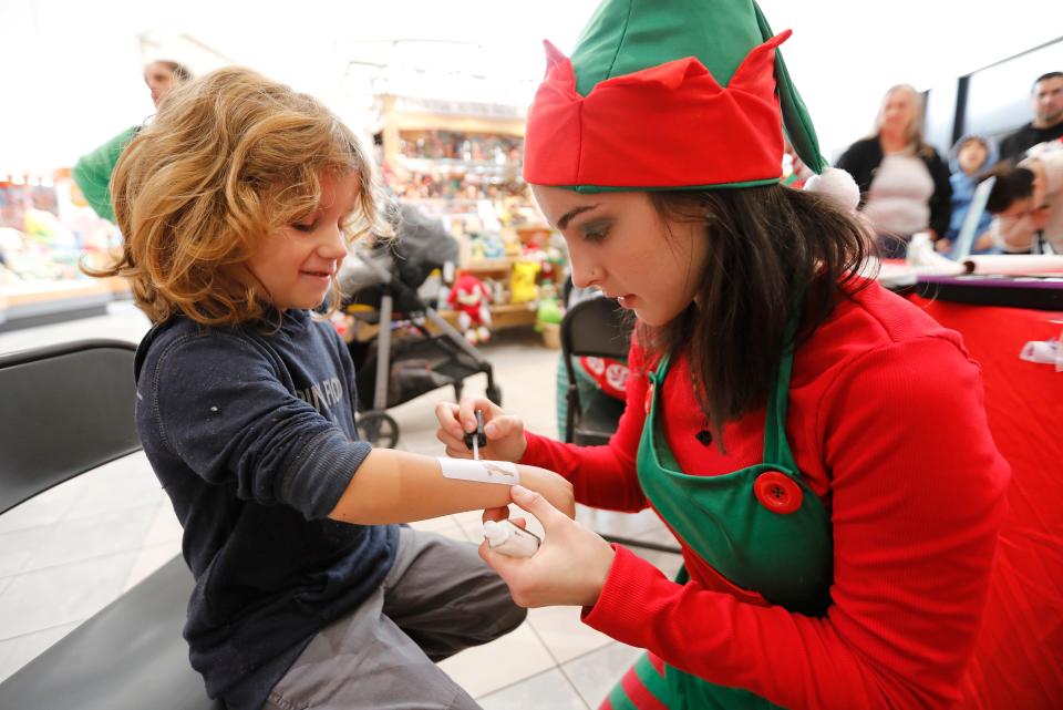 Corrina Janshejo paints a reindeer tattoo on a young boys are during Holiday crafts at the Dartmouth Mall.