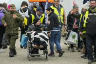 Volunteers help a refugee in a wheelchair after fleeing the war from neighboring Ukraine, at the border crossing in Medyka, southeastern Poland, Wednesday, April 6, 2022. (AP Photo/Sergei Grits)