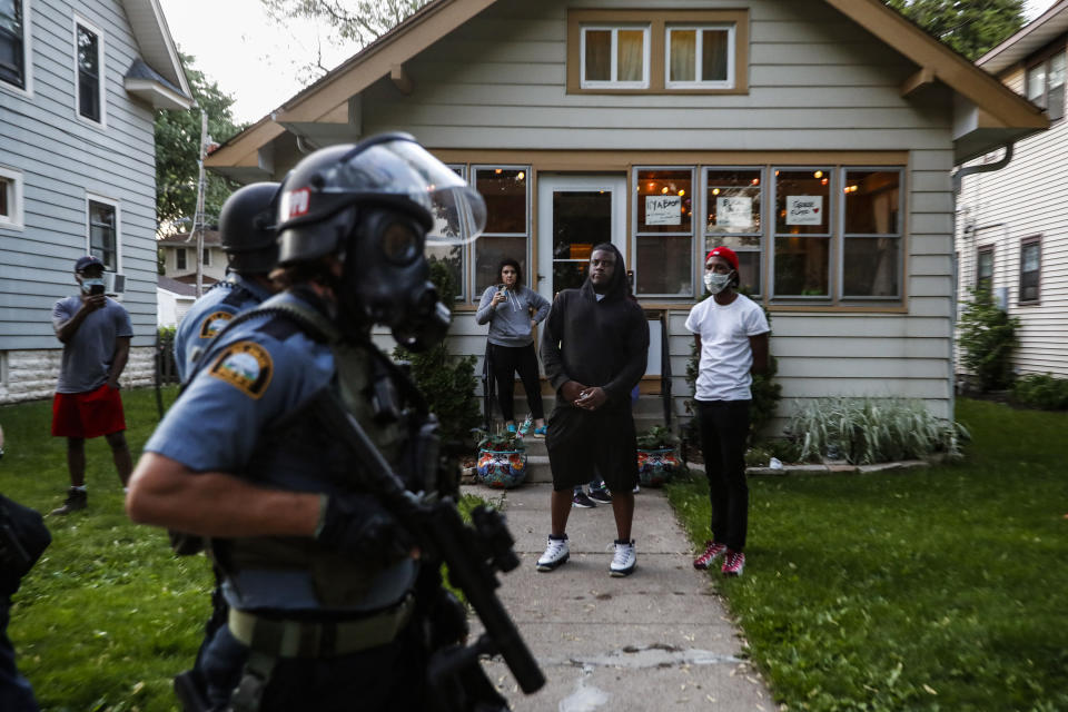 Bystanders watch as police walk down a street May 28, 2020, in St. Paul, Minn. Protests over the death of George Floyd, a black man who died in police custody, broke out in Minneapolis for a third straight night. The image was part of a series of photographs by The Associated Press that won the 2021 Pulitzer Prize for breaking news photography. (AP Photo/John Minchillo)