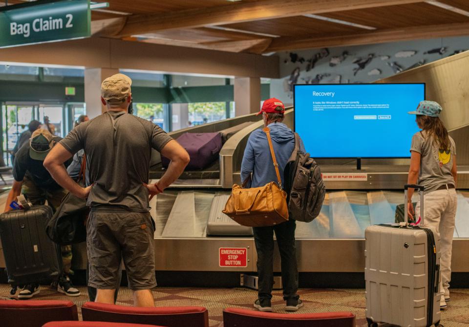 Eugene Airport passengers wait by the baggage carousel while an advertising carousel was down because of issues caused Friday by a widespread outage on Microsoft systems.