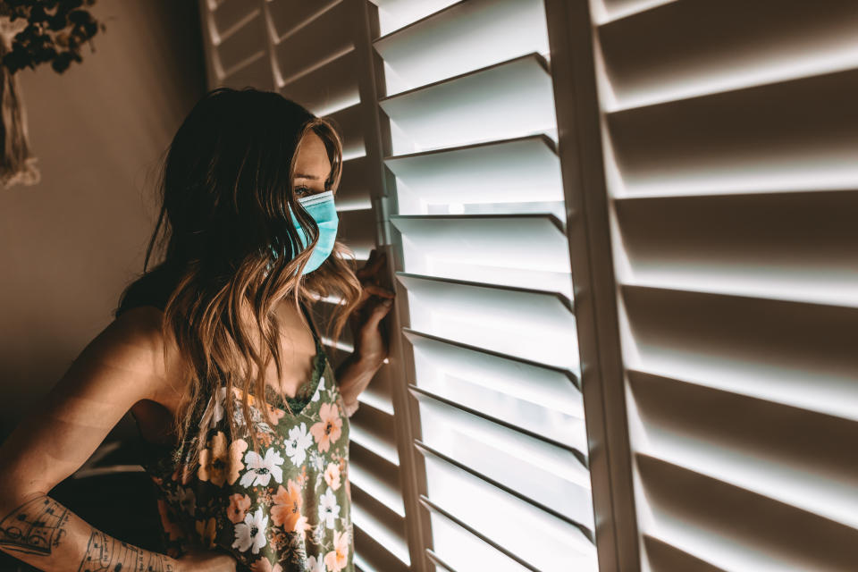 Woman with face mask in her home during stay at home order. Cleaning, and longing to get outside. COVID-19. March 2020