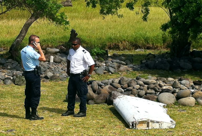 Police stand next to a piece of aircraft debris found in the coastal area of Saint-Andre de la Reunion, on the French Indian Ocean island of La Reunion, on July 29, 2015