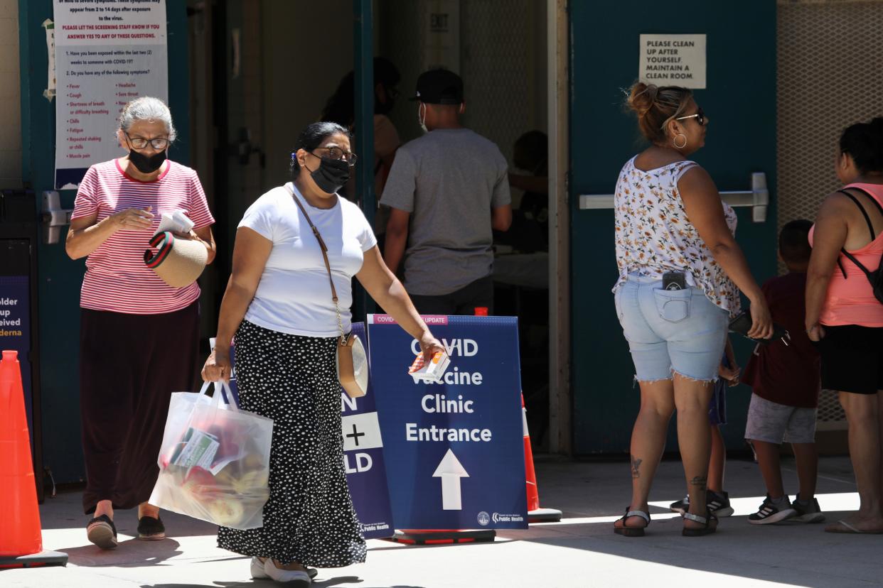 A cluster of people in face masks come in and out of a COVID-19 vaccine clinic.