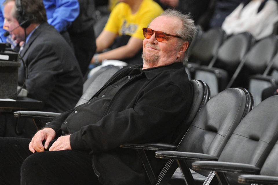 Jack Nicholson smirking as he sits courtside by himself