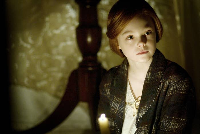 Elle Fanning as a child holds a candle and looks serious offscreen