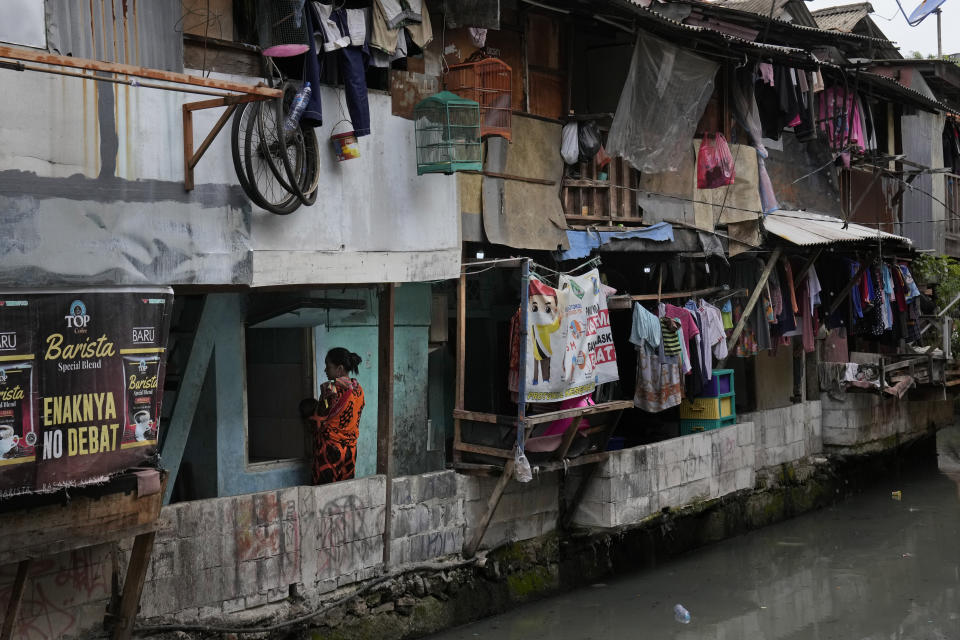 A woman carries her baby outside of her house in a low-income neighborhood next to a polluted city canal in Jakarta, Indonesia, Tuesday, Jan. 25, 2022. Indonesian parliament last week passed the state capital bill into law, giving green light to President Joko Widodo to start a $34 billion construction project this year to move the country's capital from the traffic-clogged, polluted and rapidly sinking Jakarta on the main island of Java to jungle-clad Borneo island amid public skepticism. (AP Photo/Dita Alangkara)