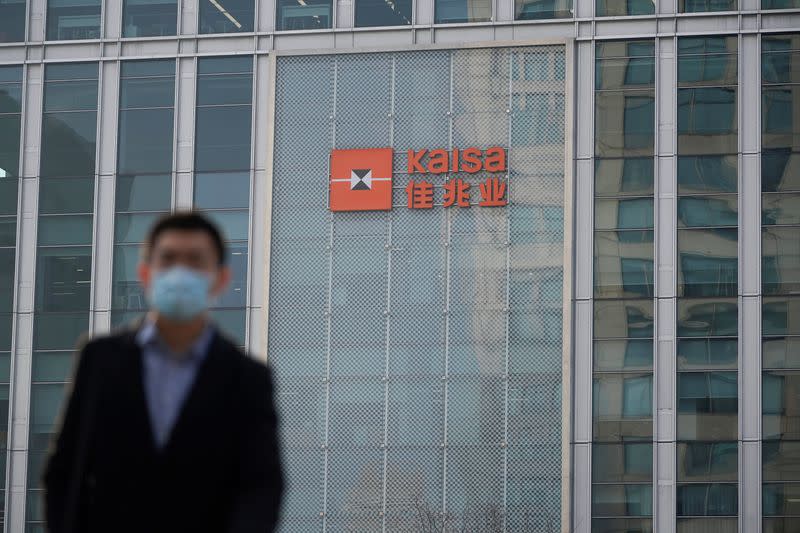 A man in a protective mask walks in front of the Shanghai Kaisa Financial Centre as a sign of the Kaisa Group Holdings is pictured in the background, in Shanghai