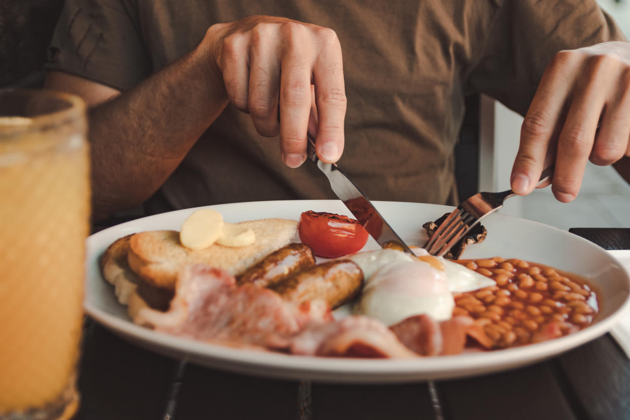 man eating an english breakfast with orange juice on a black table