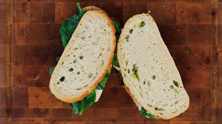 two sandwiches with spinach on wood board