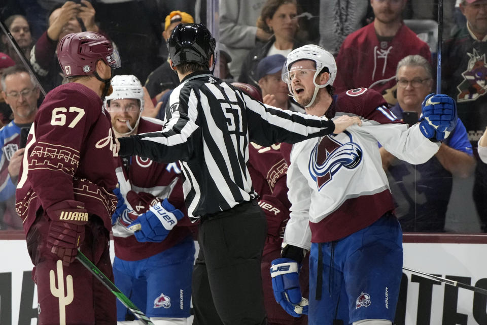 Linesman Justin Johnson (57) separates Arizona Coyotes left wing Lawson Crouse (67) and Colorado Avalanche center Ryan Johansen (12) during the third period during an NHL hockey game, Wednesday, Dec. 27, 2023, in Tempe, Ariz. (AP Photo/Rick Scuteri)