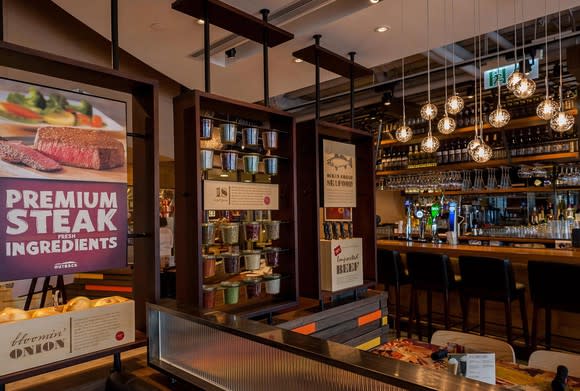 Bar area of Outback Steakhouse location, including three bar stools, a couple of small tables, and posters for products.