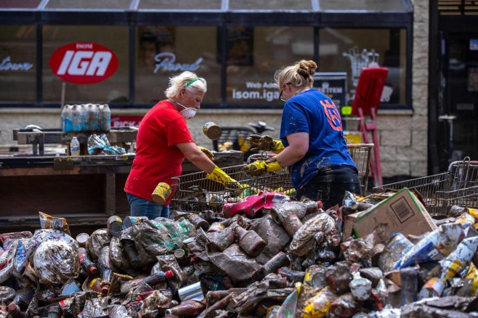 Employees at Isom IGA in Isom, Ky., throw out canned food on Monday, Aug. 1, 2022, after the business was was ravaged by historic floods. The store’s entire inventory was spoiled by the flood waters. After months of cleaning, repairs and rebuilding, the grocery store is scheduled to reopen Saturday, April 1, 2023.