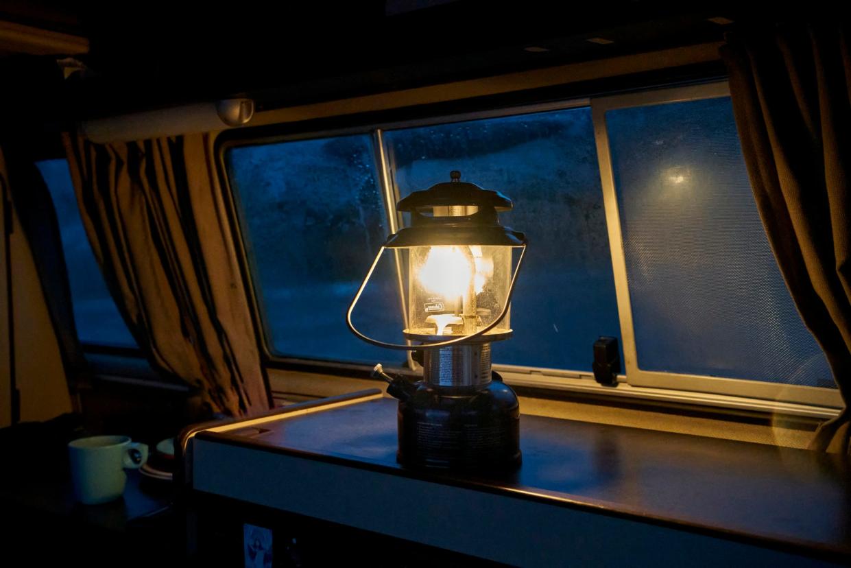 A lit gas lantern on a counter top in front of a set of windows.