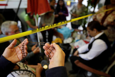 A woman offers to pray with a rosary with family members of people missing under the rubble of a collapsed building after an earthquake, in Mexico City, Mexico September 23, 2017. REUTERS/Jose Luis Gonzalez