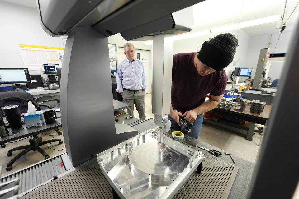 As Reata Engineering and Machine Works CEO Grady Cope looks on, a worker prepares a Hexagon machine to confirm that parts meet customers' standards, Thursday, Feb. 15, 2024, in Englewood, Colo. At Reata, which makes parts for aircraft and medical device manufacturers, "efficiency was kind of forced on us,'' Cope said. (AP Photo/David Zalubowski)