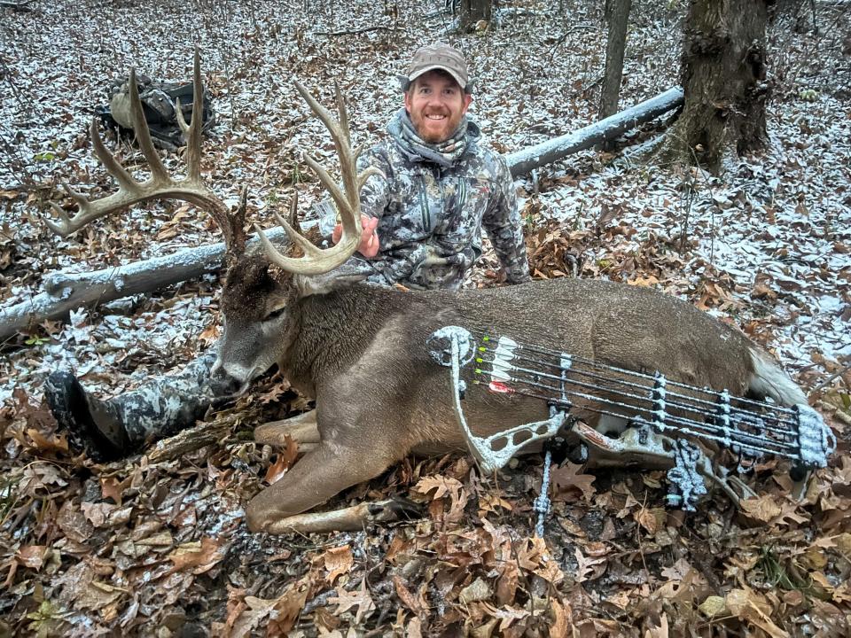 A bowhunter holds up the head of a nice buck in light snow.