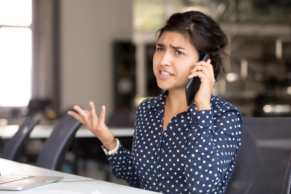 Person at a desk looks concerned while talking on the phone, with a laptop in front