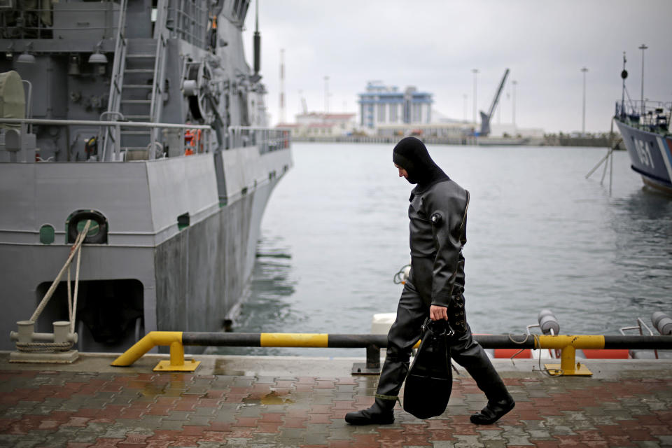 A diver carries his flippers as he boards a Russian military vessel, at left, docked in the seaport, Wednesday, Jan. 29, 2014, in Sochi, Russia, home of the upcoming 2014 Winter Olympics. (AP Photo/David Goldman)