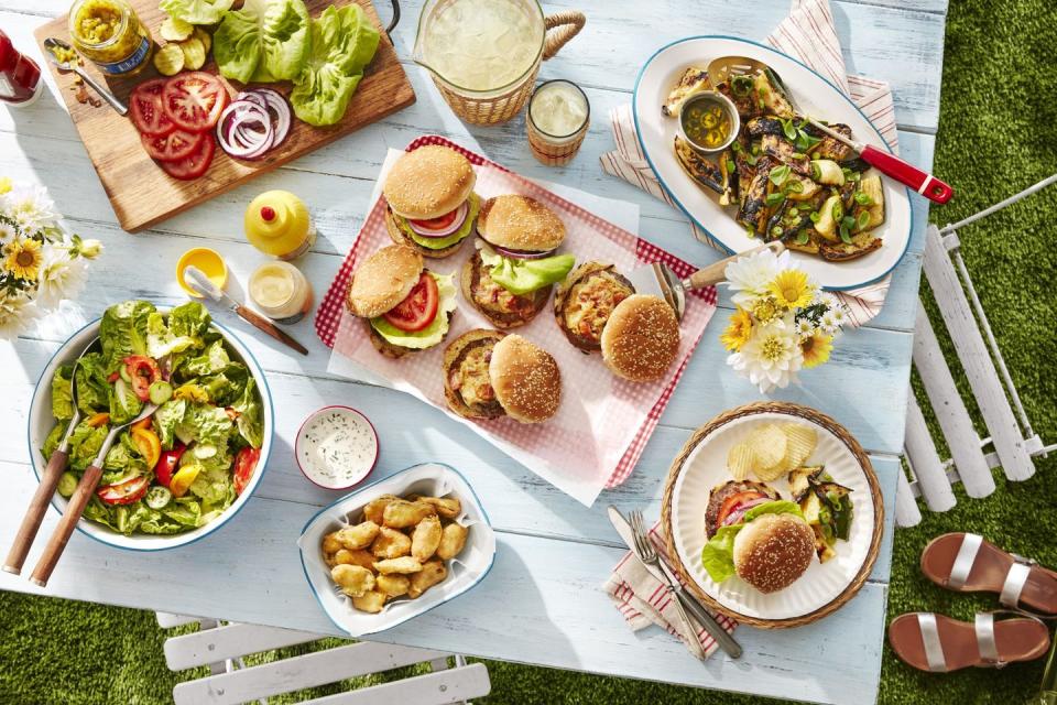 an outdoor table set with grilled burgers and other summer sides