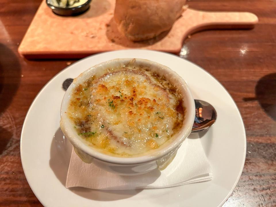 A cup of French onion soup with crusted cheese on top.