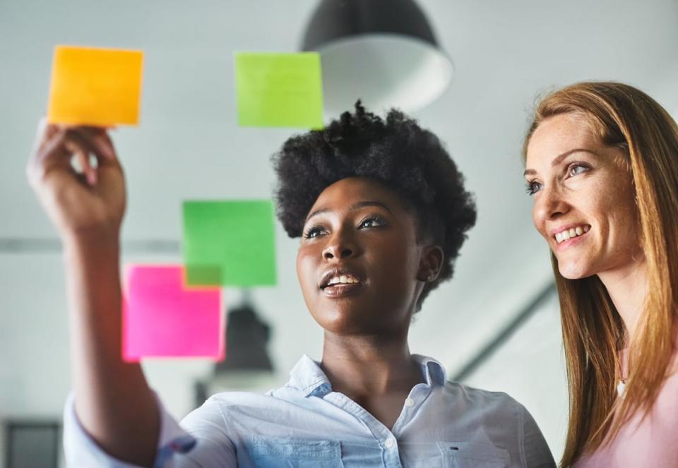 Two people smile while writing ideas on sticky notes. 