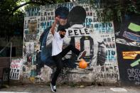 Silvio Cesar Martins plays soccer near a mural depicting Brazilian soccer legend Pele kissing the face of the comic superhero Batman in Sao Paulo