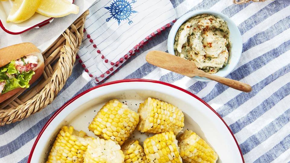 corn cobettes in a white dish with red trim and a small bowl of basil butter on the side