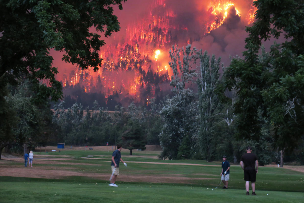 Golfers play in North Bonneville, Washington, last fall as the Eagle Creek wildfire burns. The U.N.'s Intergovernmental Panel on Climate Change said the world must drastically cut greenhouse gas emissions to avoid climate disaster. (Kirsti McCluer / Reuters)