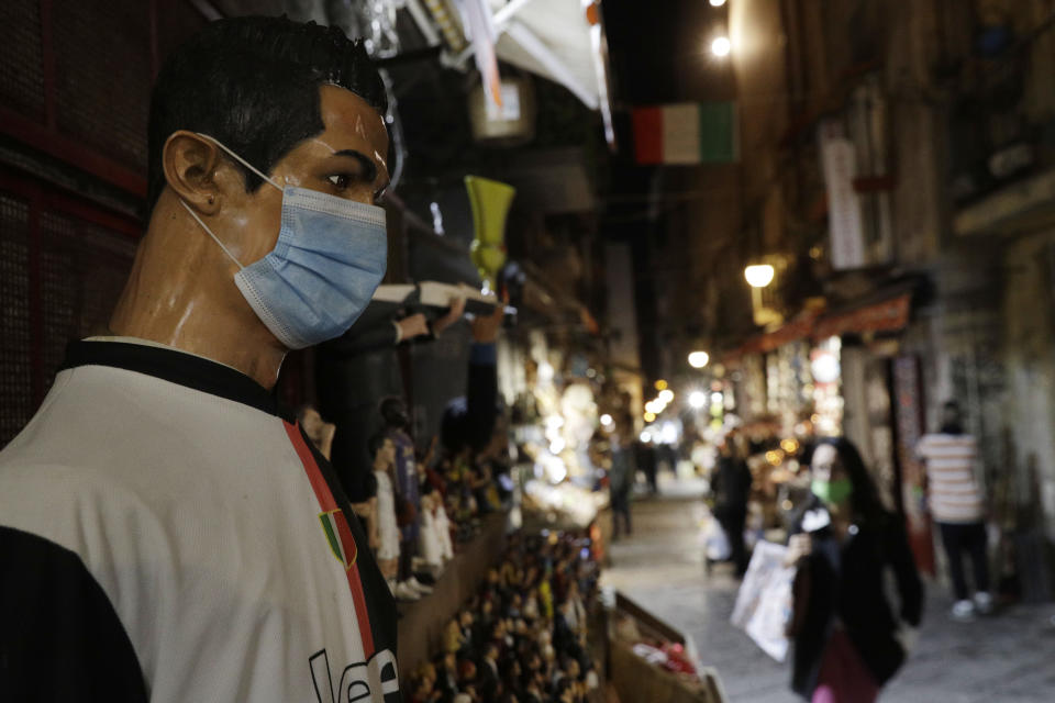 A statue of soccer star Cristiano Ronaldo, wearing a face mask, is displayed at a nativity scenes shop in San Gregorio Armeno street in Naples, Italy, Friday, Nov. 13, 2020. The regions of Campania and Tuscany were designated red zone on Friday, signaling the dire condition of a hospitals struggling with a surge of new admissions.(AP Photo/Gregorio Borgia)