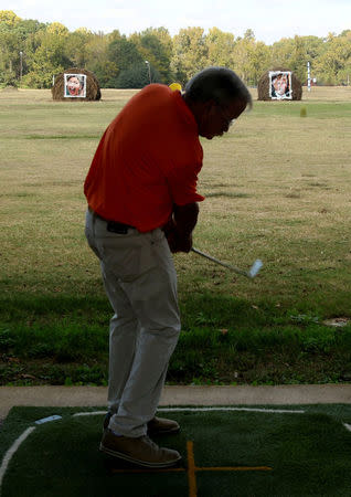 Mike Williams, owner of the Alpine Target Golf Center, shows off his swing at a driving range with hay bales covered with the portraits of U.S. presidential nominees Hillary Clinton and Donald Trump, which are used as a mock polling station, at Alpine Target Golf Center in Longview, Texas November 2, 2016. REUTERS/Todd Yates