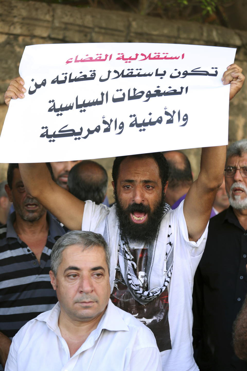 A protester chants slogans as he holds a placard in Arabic that reads, "the independence of justice is when the judiciary is independent from American political and security pressures," during a sit-in near a military court where an arrest warrant was issued for Lebanese-American Amer Fakhoury, who confessed he'd worked for Israel during its occupation of Lebanon for nearly two decades, in Beirut, Lebanon, Tuesday, Sept. 17, 2019. Fakhoury was detained after returning to his native Lebanon from the United States earlier this month. (AP Photo/Bilal Hussein)