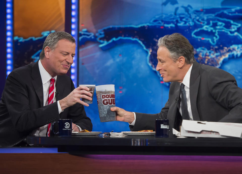 FILE- In this Feb. 3, 2014 image provided by the Mayor's Press Office, New York City Mayor Bill de Blasio, left, shares pizza and soda with host Jon Stewart on the set of Comedy Central's "The Daily Show," in New York. The image referenced de Blasio’s pizza etiquette misstep on Staten Island in January but showed that the “regular Joe” mayor is not above poking some fun at himself. (AP Photo/Rob Bennett, Mayor's Press Office, File)