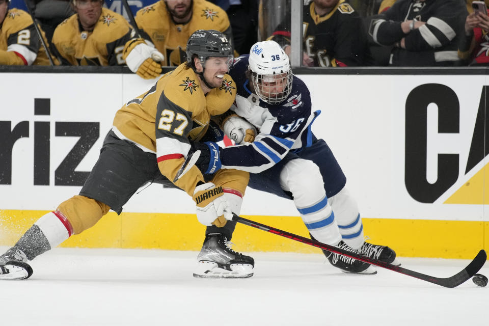 Vegas Golden Knights defenseman Shea Theodore (27) and Winnipeg Jets center Morgan Barron (36) vie for the puck during the third period of Game 1 of an NHL hockey Stanley Cup first-round playoff series Tuesday, April 18, 2023, in Las Vegas. (AP Photo/John Locher)