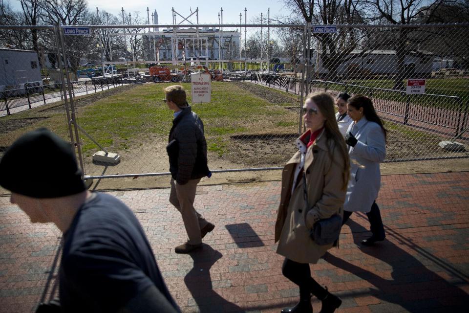 In this photo taken Feb. 17, 2017, pedestrians walk along fencing erected in Lafayette Park, across from the White House in Washington, as work continues with the dismantling of the presidential inauguration reviewing stand. (AP Photo/Pablo Martinez Monsivais)