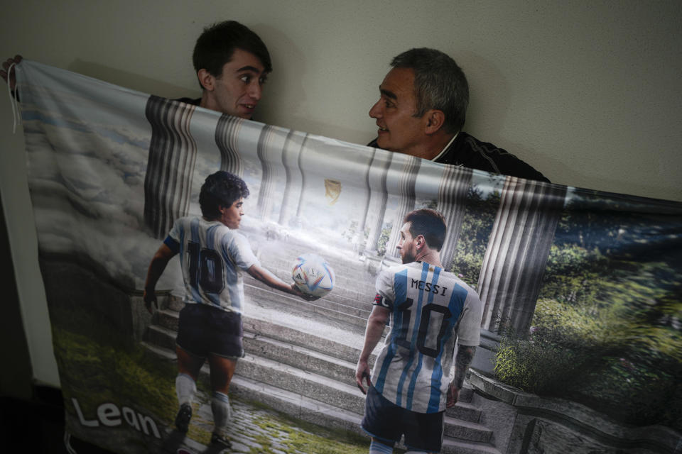Osvaldo Santander y su hijo Julián posan con una pancarta con las imágenes del fallecido astro Diego Maradona y Lionel Messi en su residencia en Buenos Aires, Argentina, el jueves 18 de agosto de 2022. (A Foto/Natacha Pisarenko)